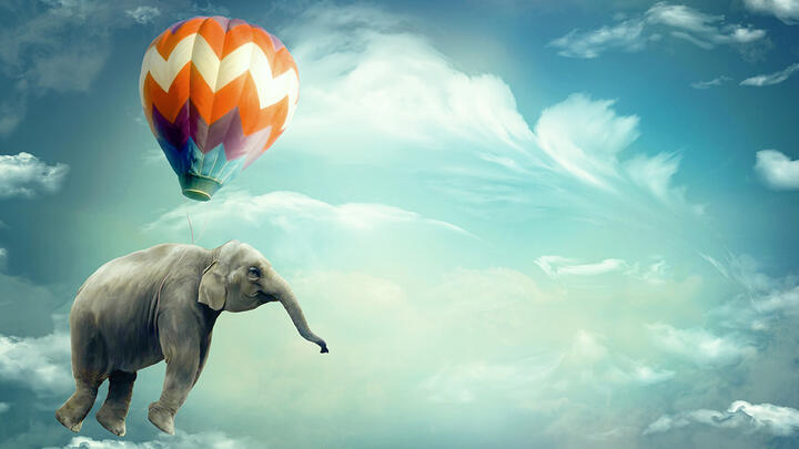 An elephant carried by a hot air ballon in a beautiful blue sky
